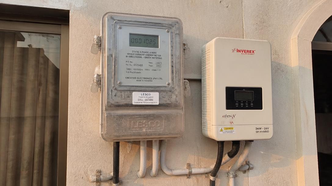 Pakistani DISCO bidirectional net meter mounted beside a solar inverter on a house wall